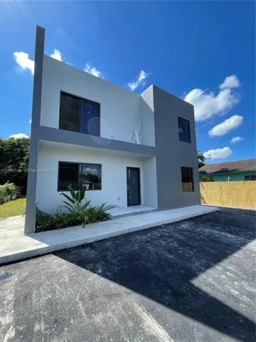 Modern two-story exterior featuring a high-contrast stucco facade, clean geometric lines, dark-framed glass windows, and a paved driveway
