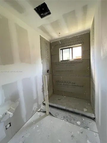 Interior space featuring installed cement board shower surrounds, a single-pane window, and pre-plumbed utility lines