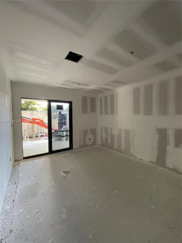 Interior space featuring unfinished drywall and a black-framed sliding glass door