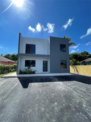 Modern two-story exterior featuring a dual-tone facade, flat roofline, paved driveway, and second-level balcony