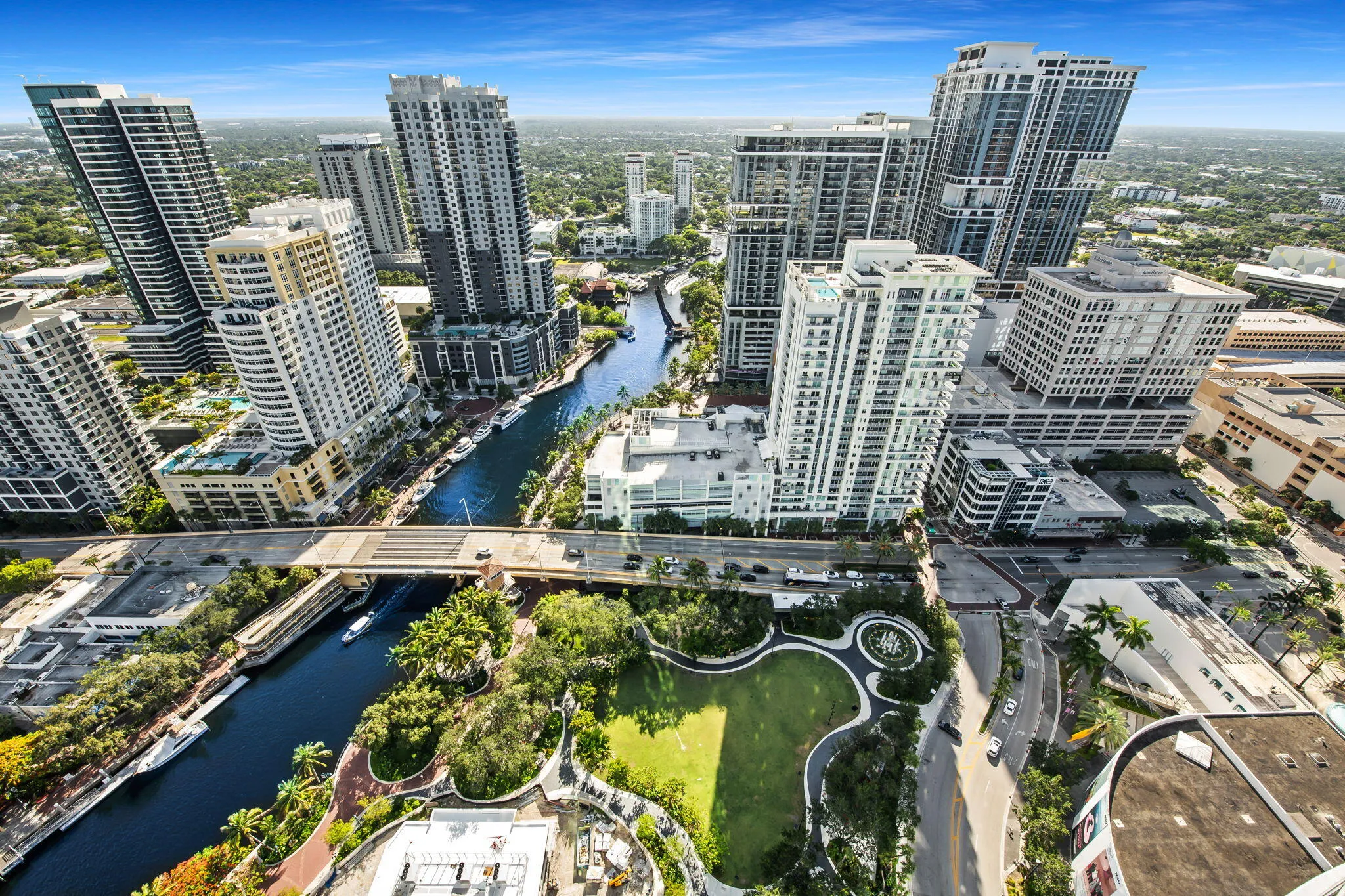 Aerial perspective of a vibrant metropolitan area featuring a river, multiple high-rise buildings, extensive green spaces, and prominent roadways