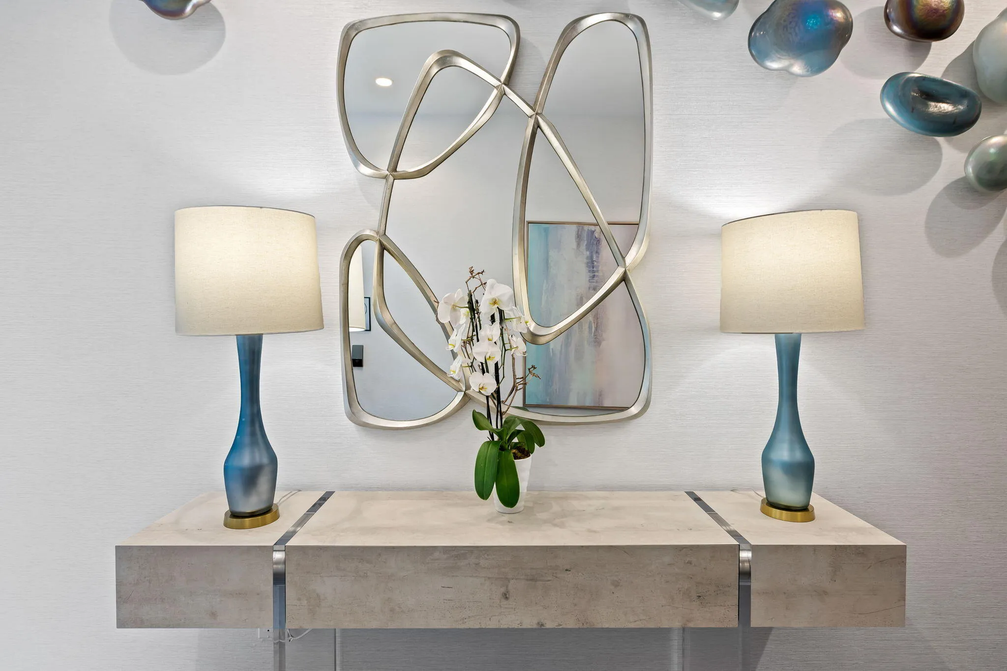 Floating console table featuring a light-toned surface with metallic accents, contemporary wall mirror with a sculptural frame, and textured wall finish
