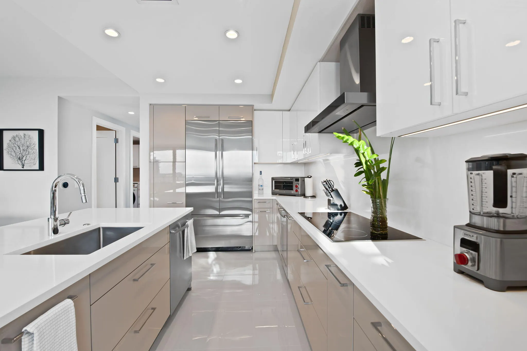 Sleek kitchen featuring an integrated stainless steel refrigerator, white countertops, and a modern cooktop with an overhead exhaust hood