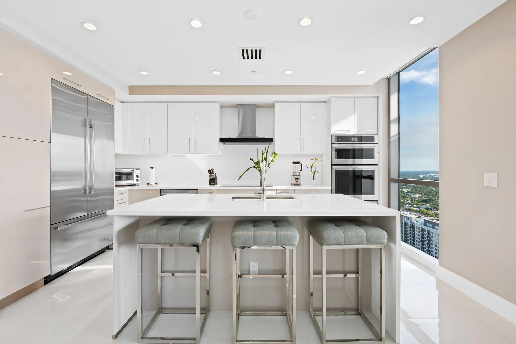 Modern kitchen featuring a large central island with seating, stainless steel appliances, white cabinetry, recessed lighting, and expansive window lines