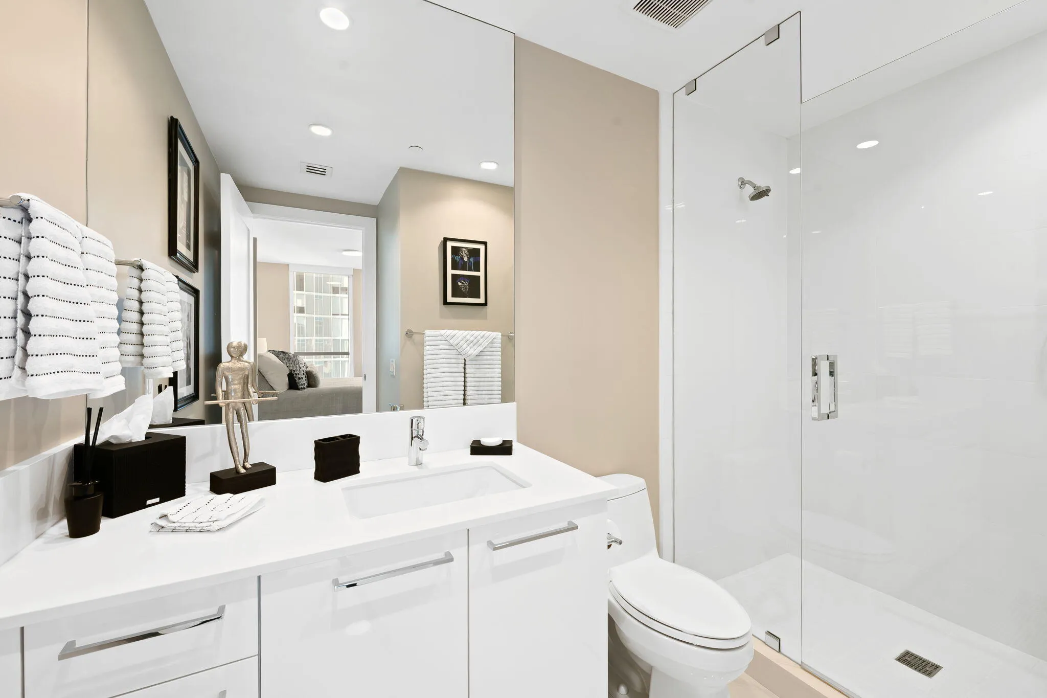 Modern bathroom featuring a frameless glass shower enclosure, a single vanity with an integrated sink, white cabinetry with chrome hardware, and a large wall-mounted mirror