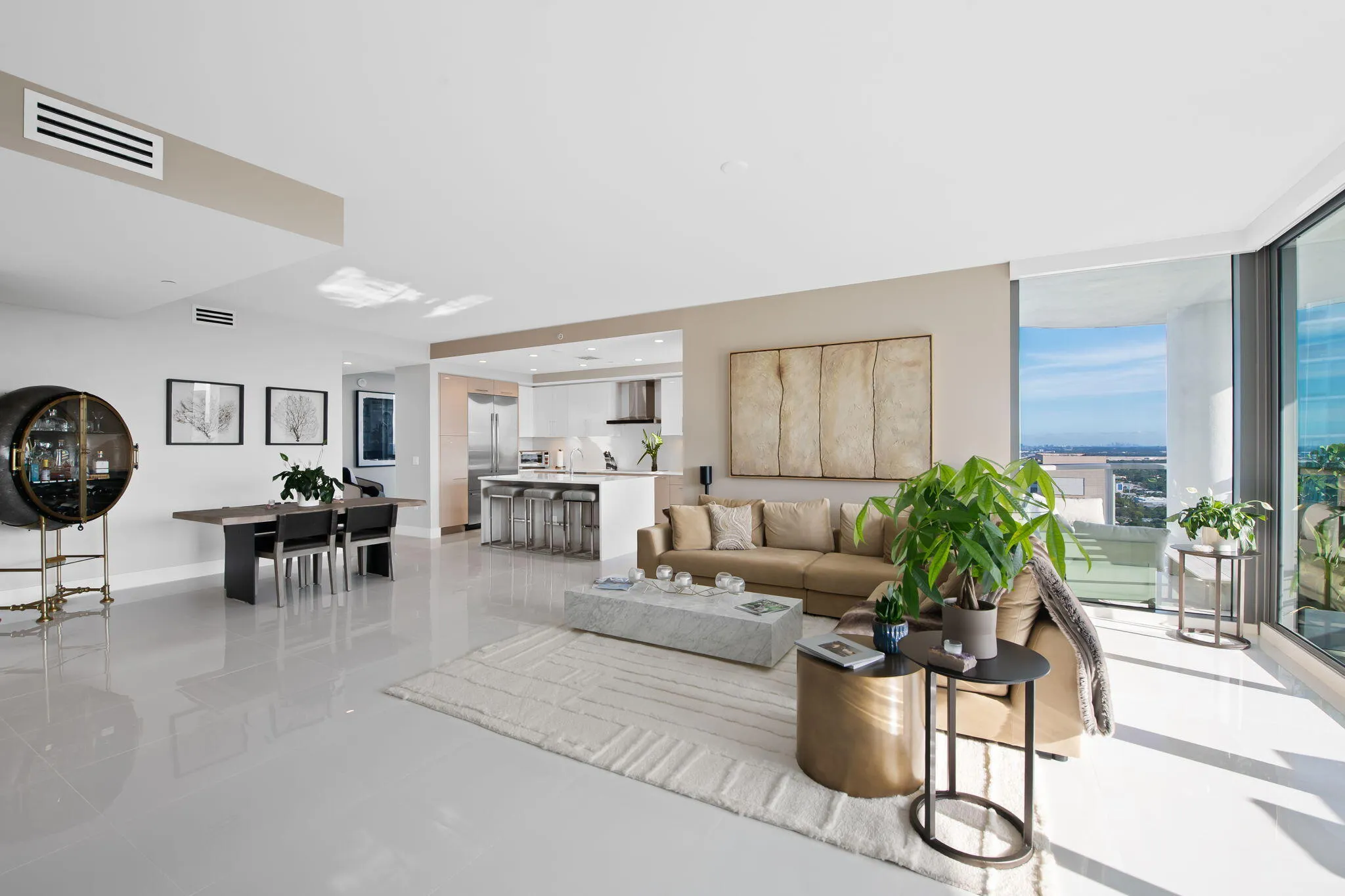 Spacious open-concept living area featuring light-toned flooring, a modern kitchen with an island, a dedicated dining space, and floor-to-ceiling windows