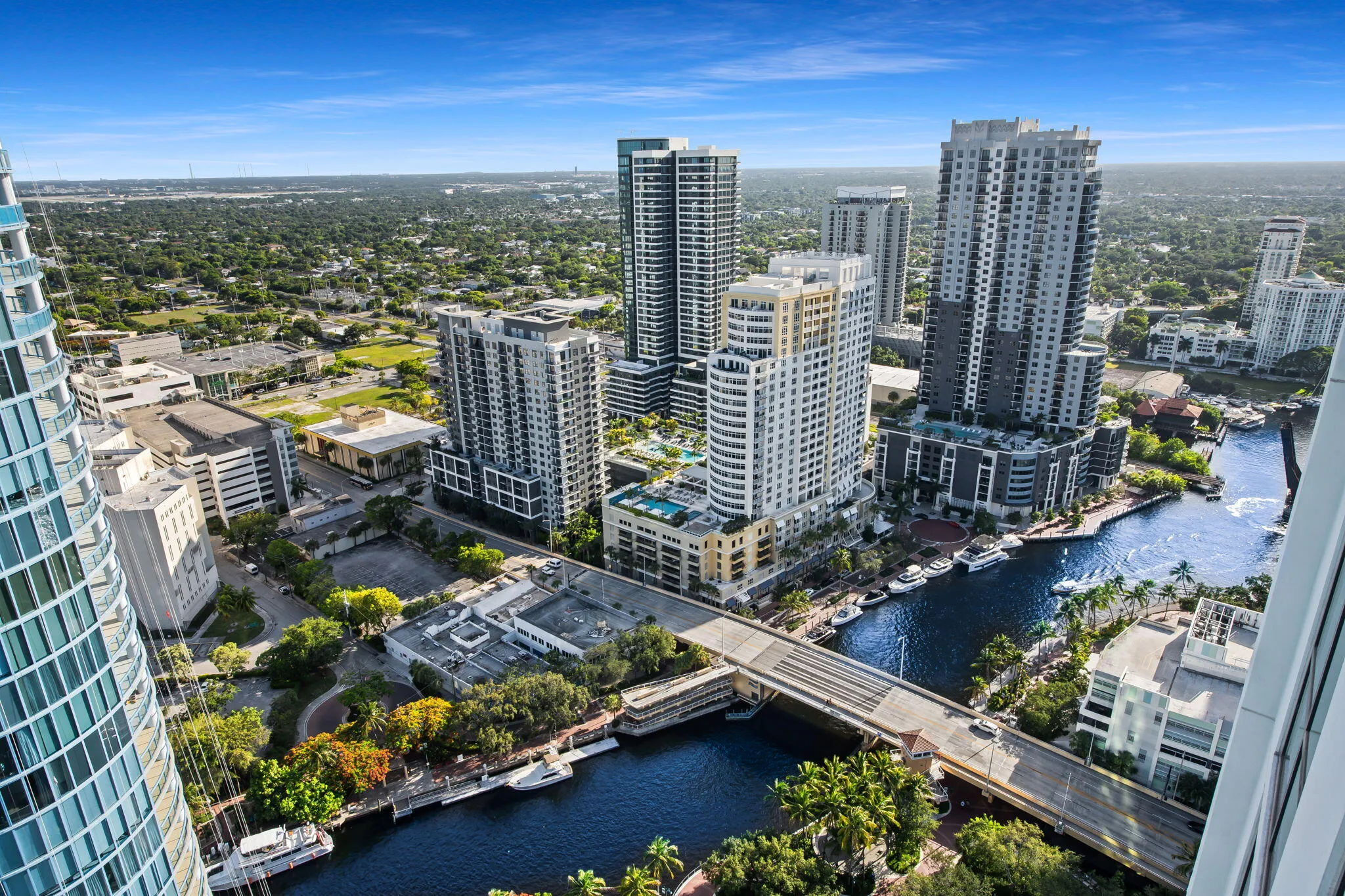 Urban waterside setting featuring multiple high-rise structures, a waterway with docked boats, and a prominent bridge