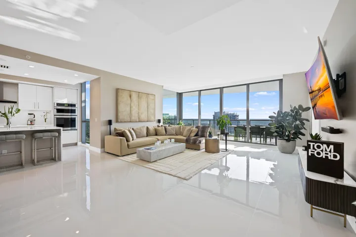 Open-concept living space featuring high-gloss tile flooring, a contemporary kitchen with white cabinetry and built-in appliances, and expansive floor-to-ceiling windows
