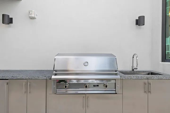 Outdoor kitchen featuring a built-in stainless steel grill, integrated sink with a gooseneck faucet, granite-finish countertop, and stainless steel cabinetry