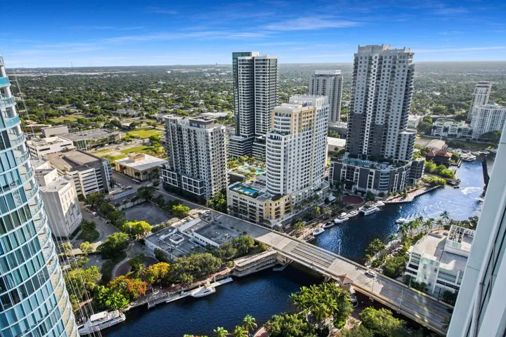 Urban waterside setting featuring multiple high-rise structures, a waterway with docked boats, and a prominent bridge