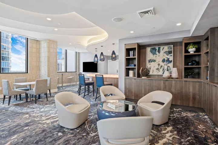 Elegant communal space featuring a built-in bar, wood-finish cabinetry with integrated shelving, and a patterned carpet