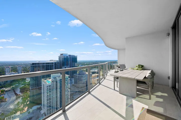 Expansive curved balcony featuring glass railings, light-toned tile flooring, and a sliding glass door entry