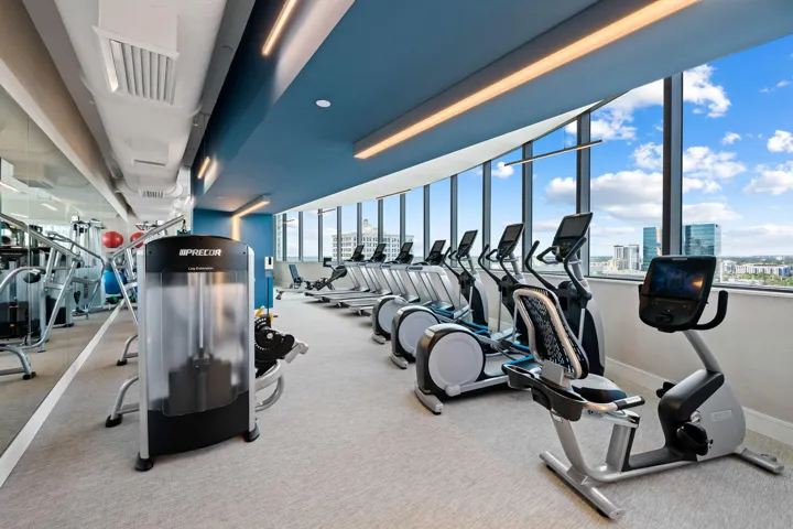 Fitness center featuring floor-to-ceiling windows, cardio equipment, strength training machines, track lighting, and a mirrored wall