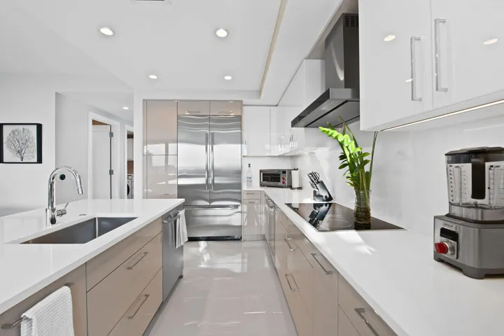 Sleek kitchen featuring an integrated stainless steel refrigerator, white countertops, and a modern cooktop with an overhead exhaust hood