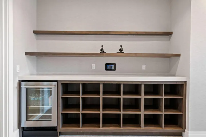 Built-in beverage station featuring a stainless steel refrigerator, white countertop, and integrated wood-finish shelving