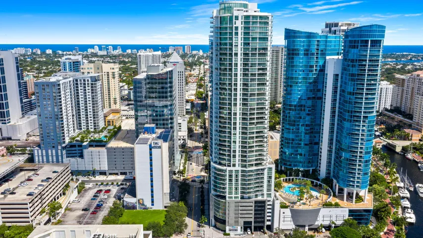 Modern high-rise architecture featuring blue-tinted glass facades, multiple balconies, a rooftop pool deck, and a canal with docked boats