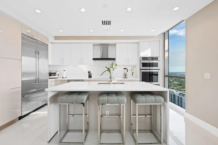 Modern kitchen featuring a large central island with seating, stainless steel appliances, white cabinetry, recessed lighting, and expansive window lines