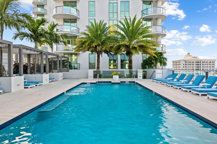 Rooftop pool deck featuring an in-ground swimming pool, multiple cabanas with slatted pergolas, and a perimeter of tropical palm trees