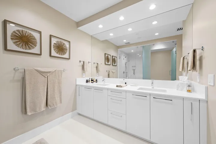 Dual vanity with white cabinetry, integrated sinks, chrome fixtures, and a spacious wall-mounted mirror