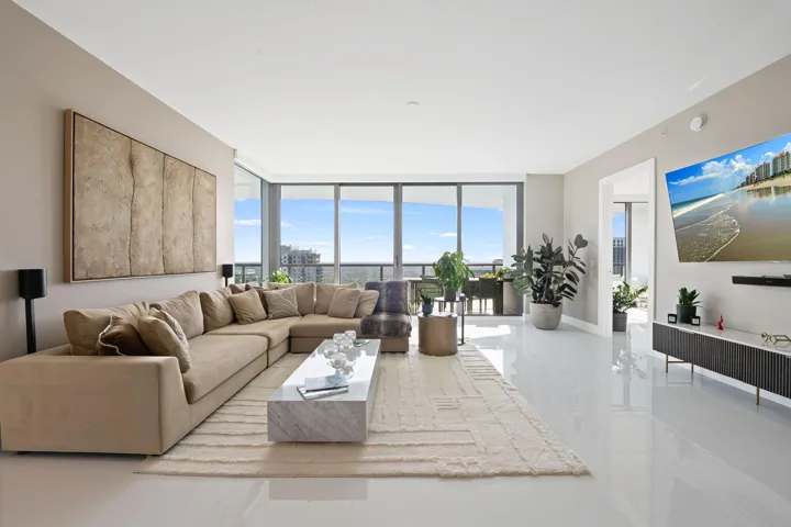 Open-concept living area with expansive floor-to-ceiling windows, showcasing a contemporary white flooring, a built-in entertainment console, and a large doorway