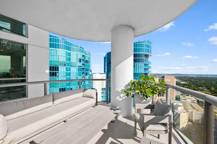 Curved balcony with glass railing, providing expansive city and distant landscape elements