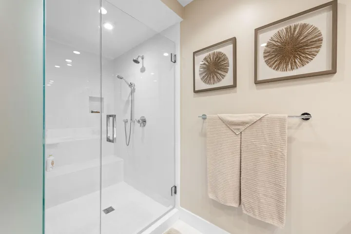 Glass-enclosed shower featuring a built-in bench, recessed shelf, and dual showerheads