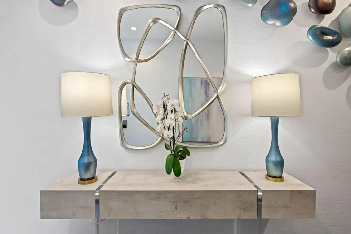 Floating console table featuring a light-toned surface with metallic accents, contemporary wall mirror with a sculptural frame, and textured wall finish
