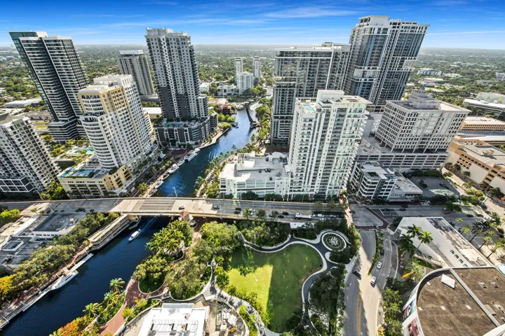 Aerial perspective of a vibrant metropolitan area featuring a river, multiple high-rise buildings, extensive green spaces, and prominent roadways