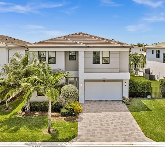 Two-story contemporary residence featuring a tiled roof, paver driveway, integrated garage, manicured landscaping, and exterior wall sconces