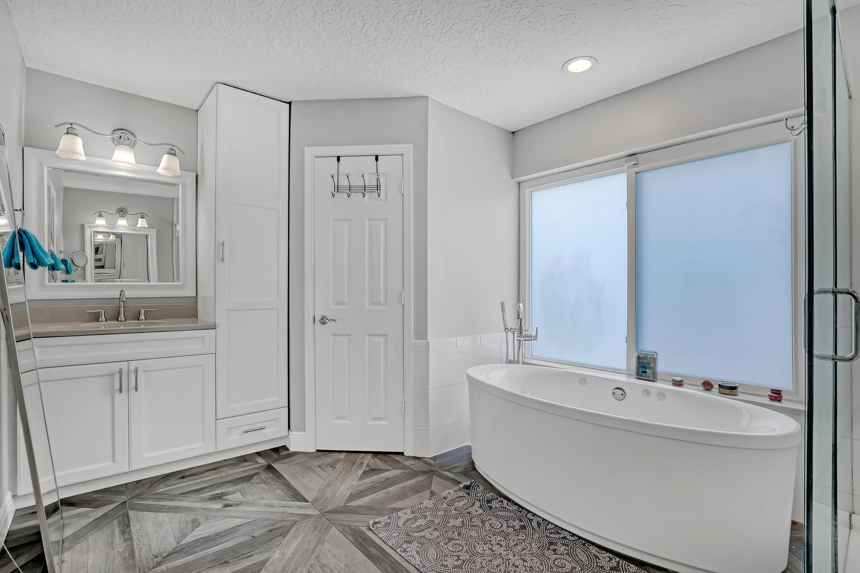 Contemporary bathroom featuring a freestanding soaking tub, frosted window, glass-enclosed shower, single vanity with integrated sink, and patterned wood-finish flooring