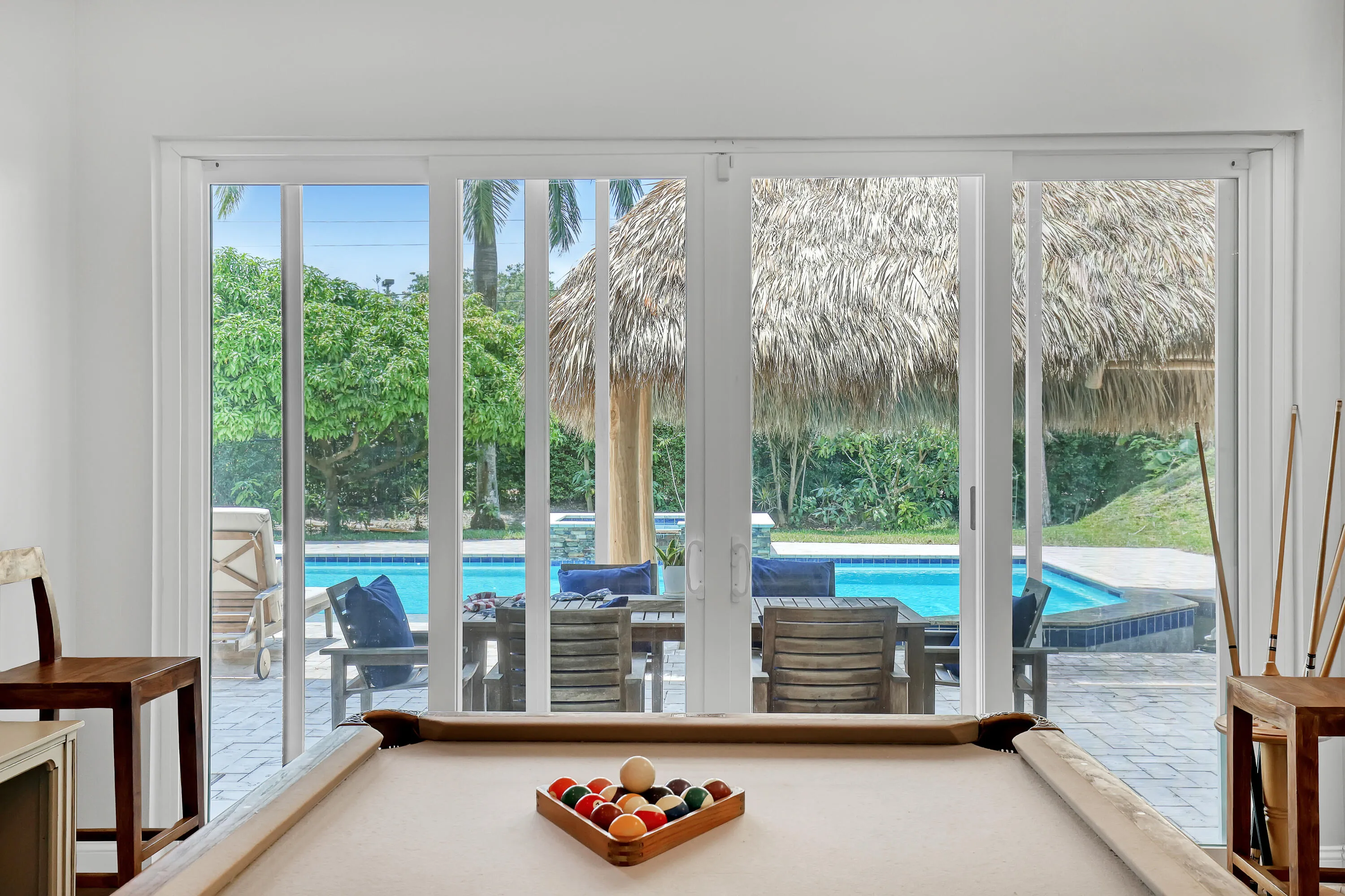 Expansive sliding glass doors open to a paver patio with a swimming pool and hot tub