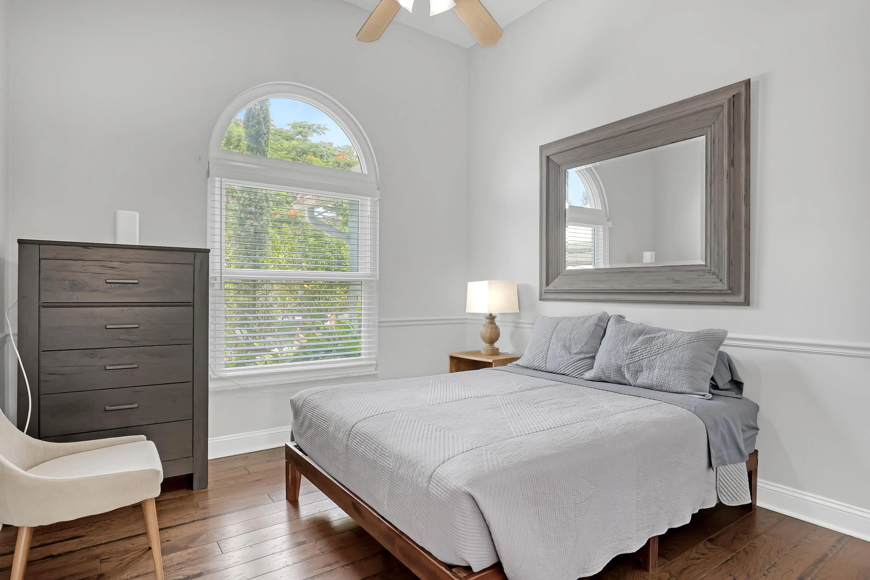 Room featuring a tall arched window with blinds, wood-finish flooring, a ceiling fan, and decorative wall molding
