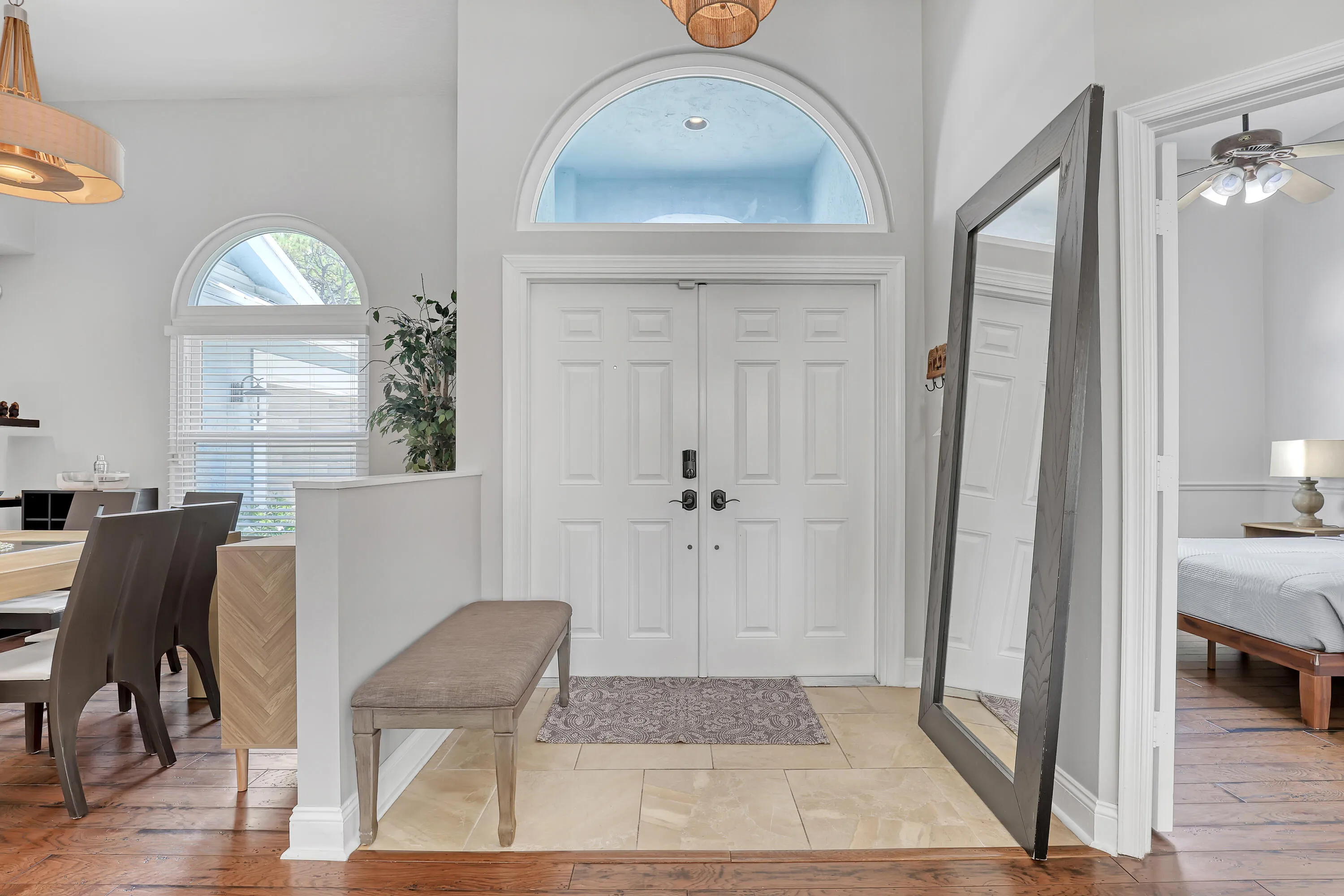 Double entry doors with an arched transom window, set above a tiled entryway with wood-finish flooring