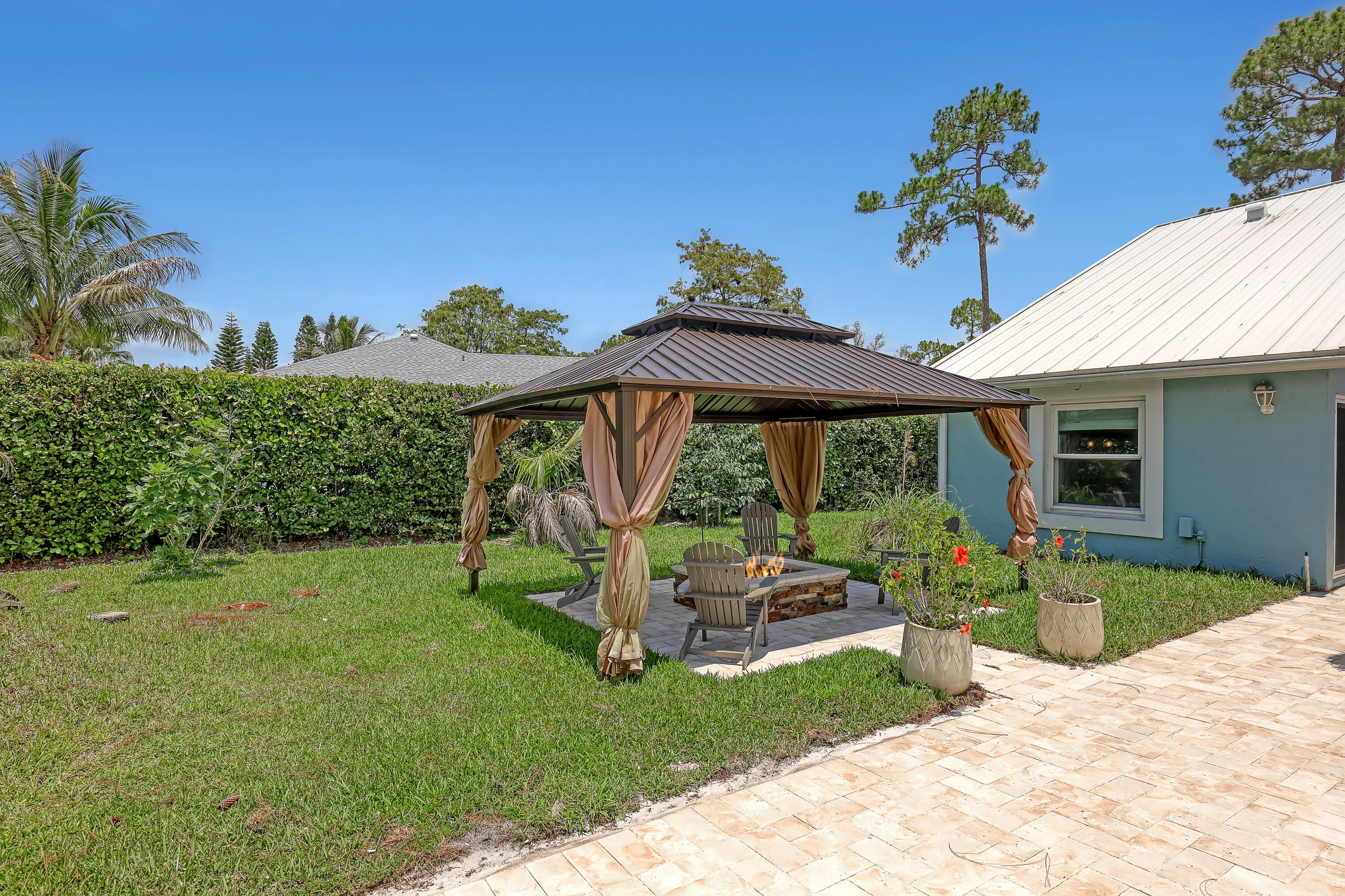 Outdoor entertaining area featuring a metal-roofed gazebo with privacy drapes, a built-in stone fire pit, and a paver patio