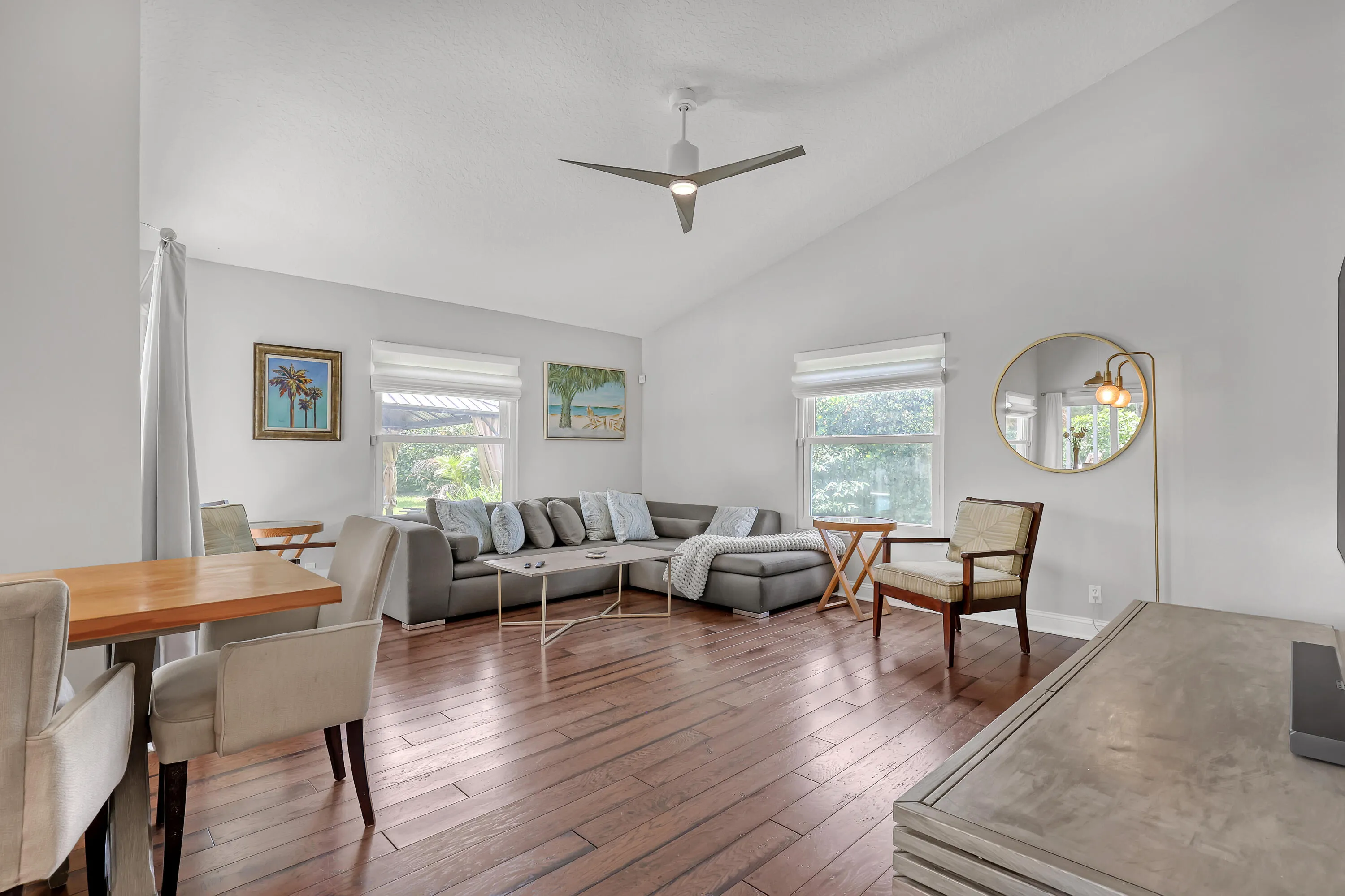 Vaulted ceiling living space with wood-finish flooring, a modern ceiling fan, and multiple windows