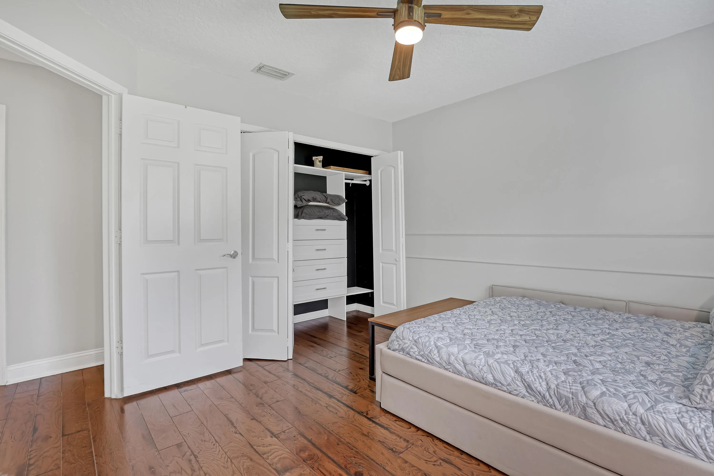 Bedroom featuring warm wood-finish flooring, a ceiling fan with integrated lighting, and a built-in closet system with drawers and shelving