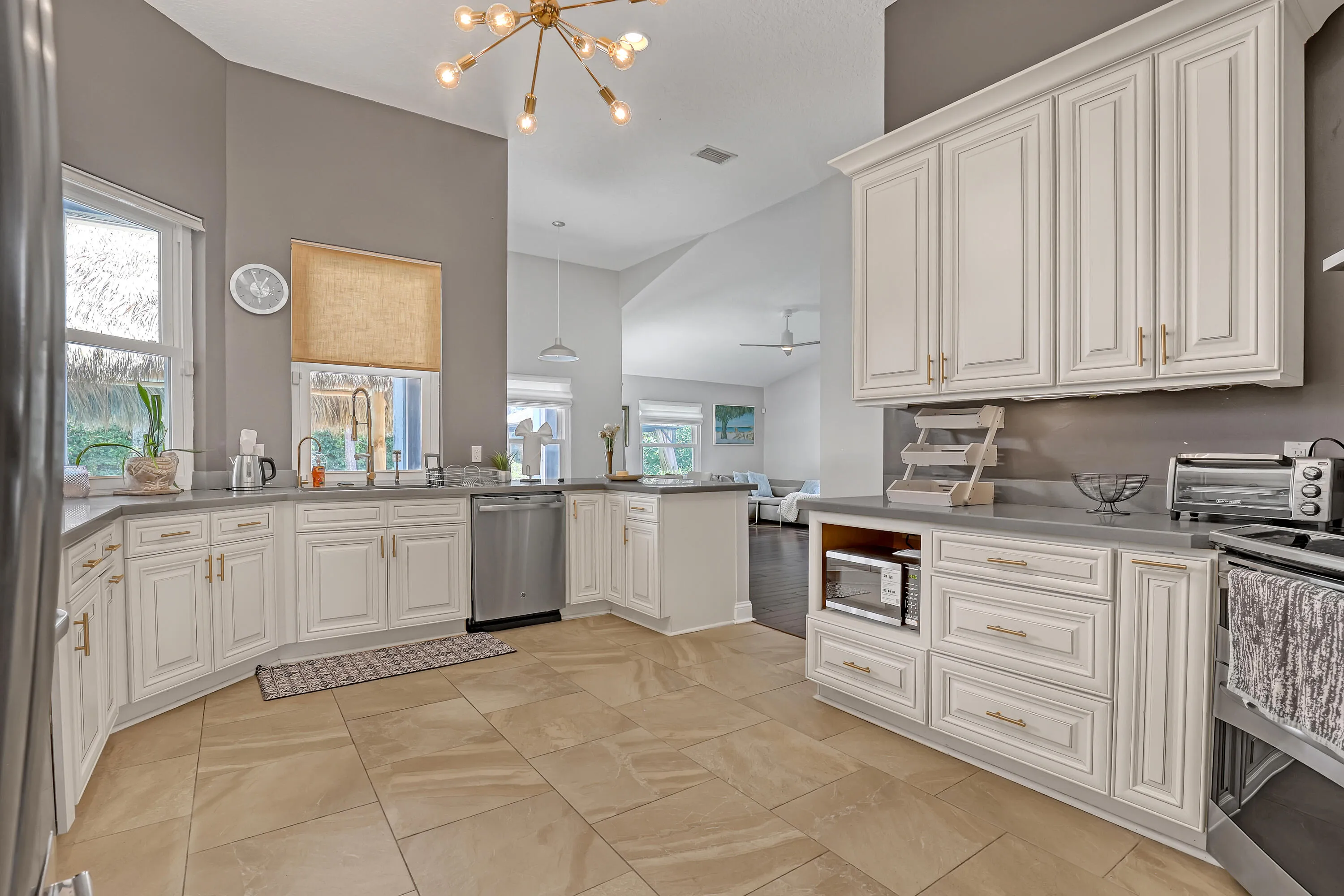 Spacious kitchen featuring extensive white cabinetry, light-toned tile flooring, light gray countertops, stainless steel dishwasher, and a contemporary ceiling light fixture