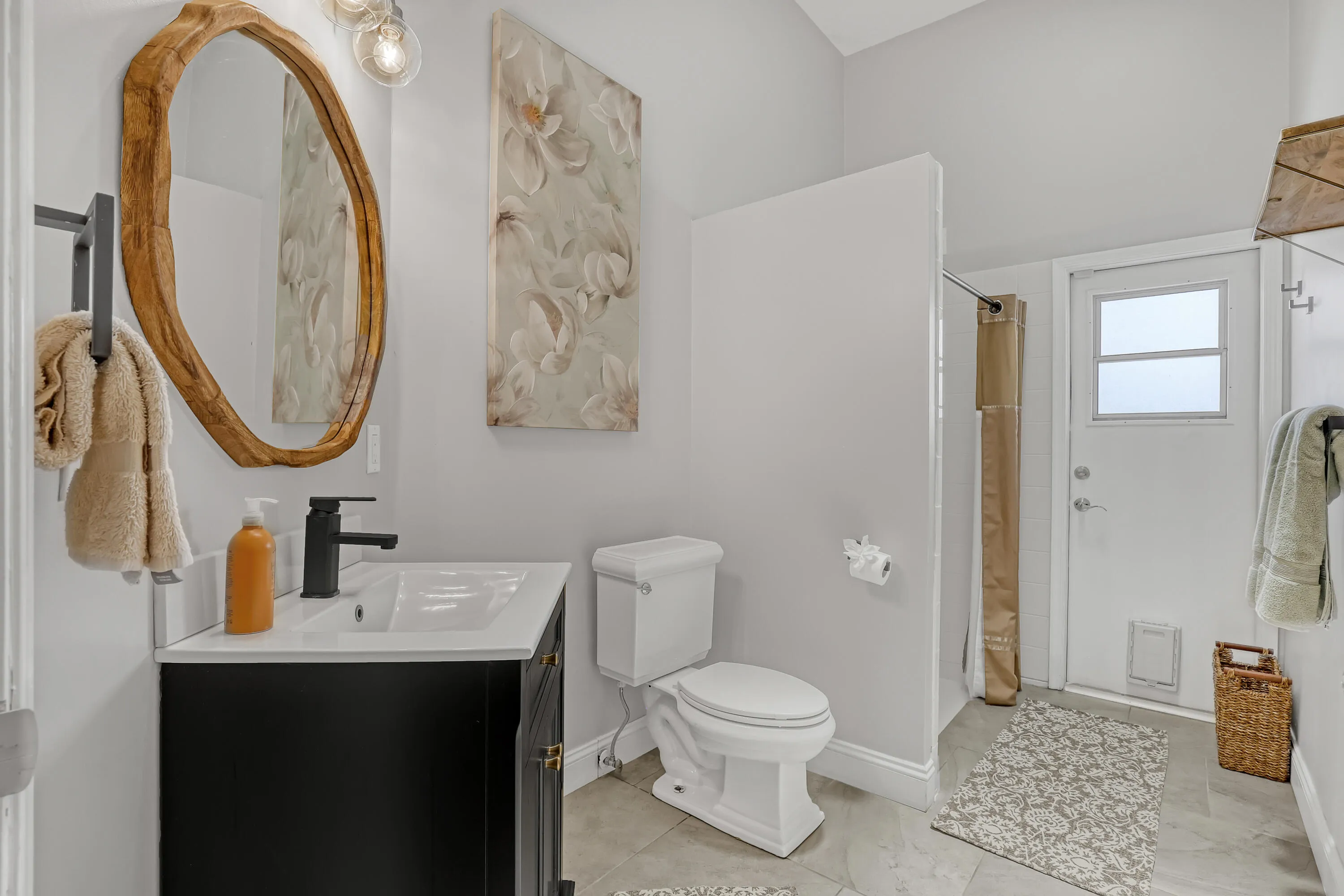 White bathroom featuring a black vanity with a white countertop and rectangular sink, matte black faucet, and a large wood-finish framed mirror