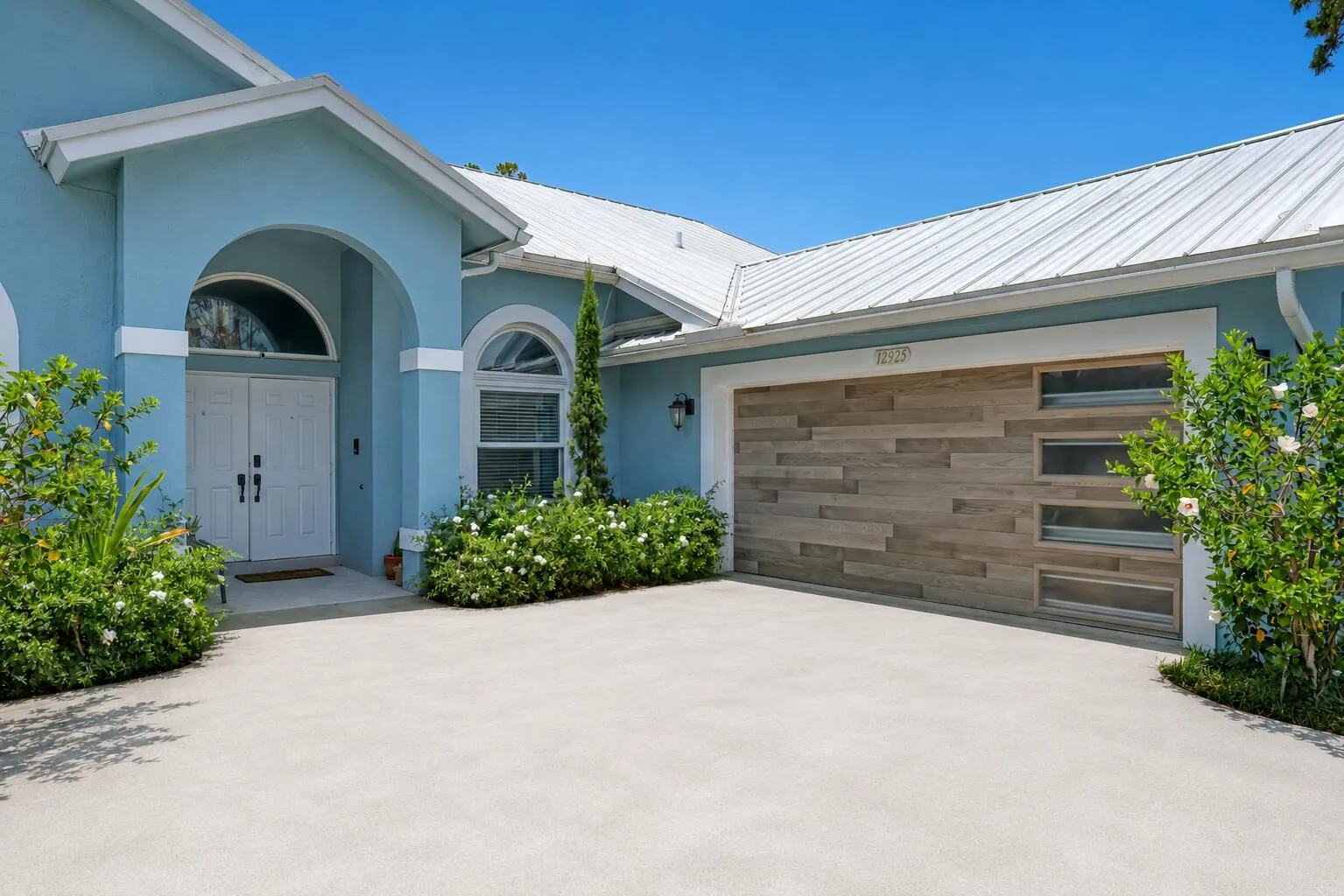 Exterior featuring a light blue stucco finish, a white metal roof, and a two-car garage with a wood-finish door and frosted windows