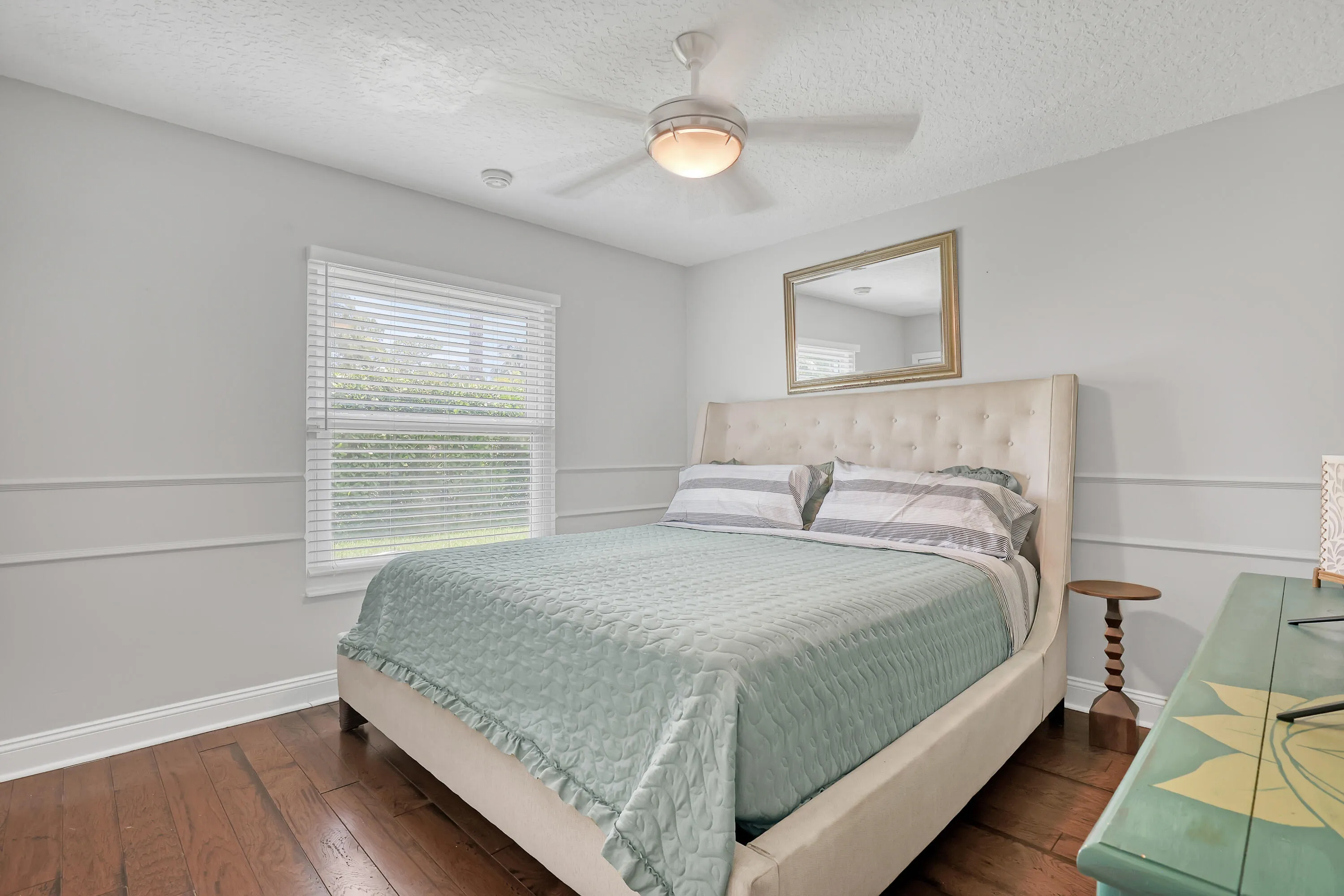 Bedroom featuring wood-finish flooring, a ceiling fan with integrated lighting, and a single window with blinds