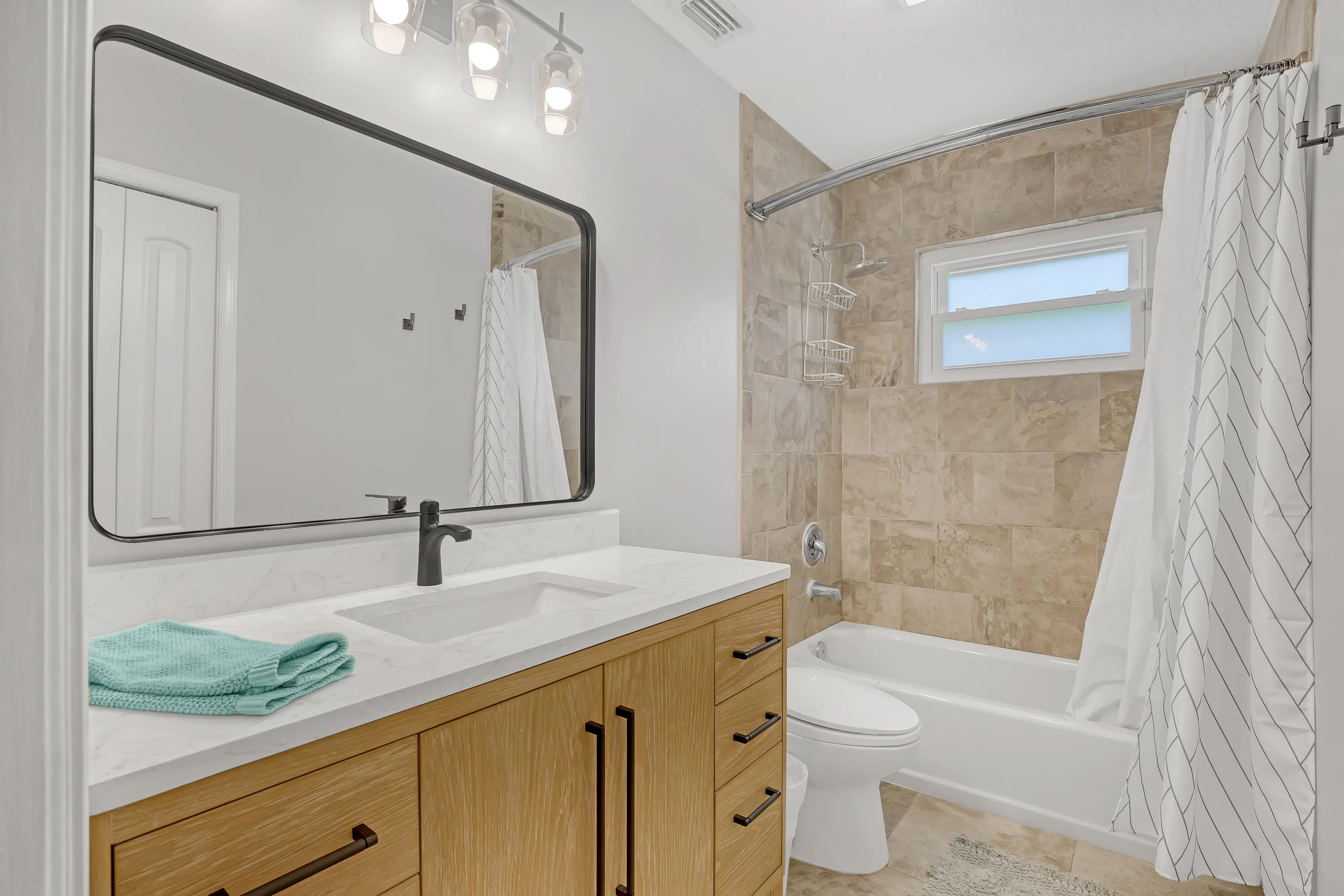Bathroom featuring a modern wood-finish vanity with a white countertop and integrated sink, a rectangular black-framed mirror, and a three-light vanity fixture