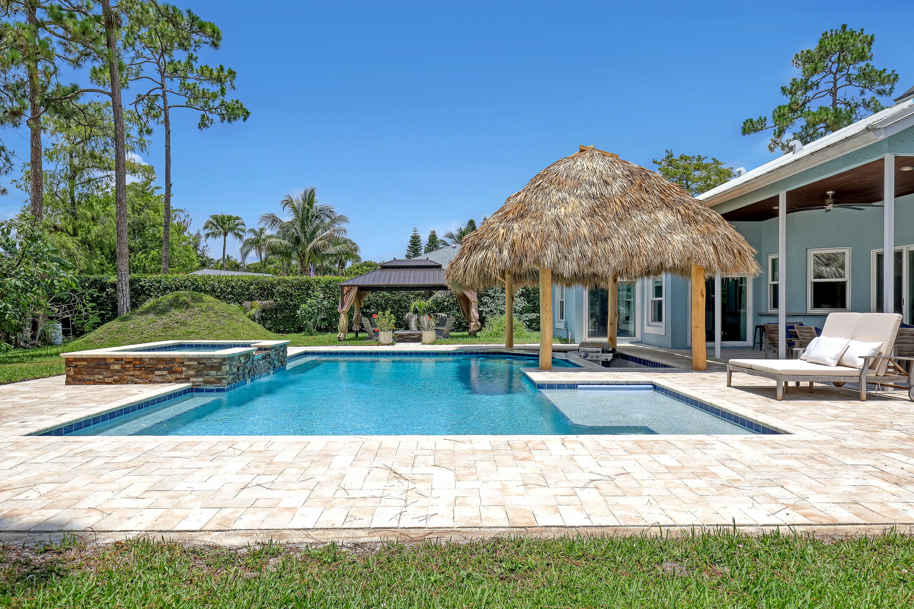 Expansive outdoor area featuring a swimming pool, integrated spa with stone surround, and a thatched-roof tiki hut