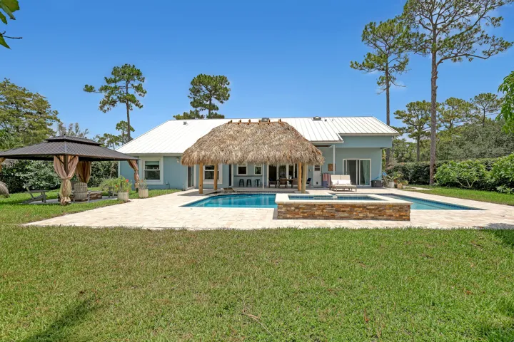Expansive backyard featuring a swimming pool, integrated spa with stone surround, and a thatched-roof tiki hut