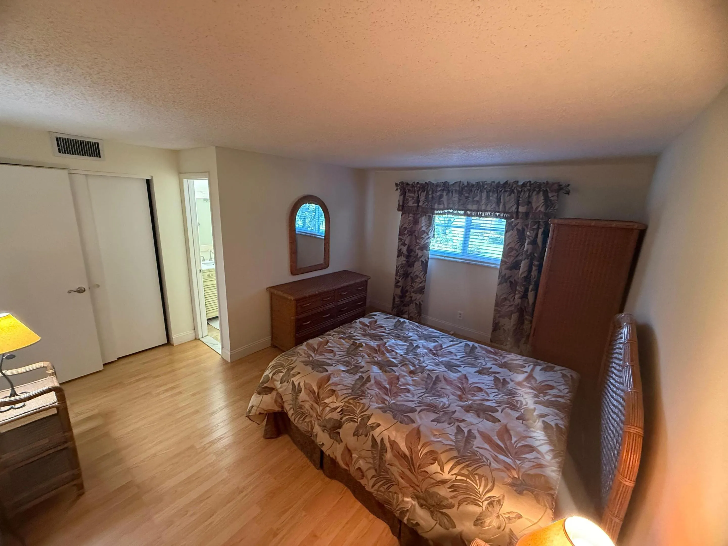 Room with light wood-finish flooring, a window with blinds, and a built-in wall air conditioning vent