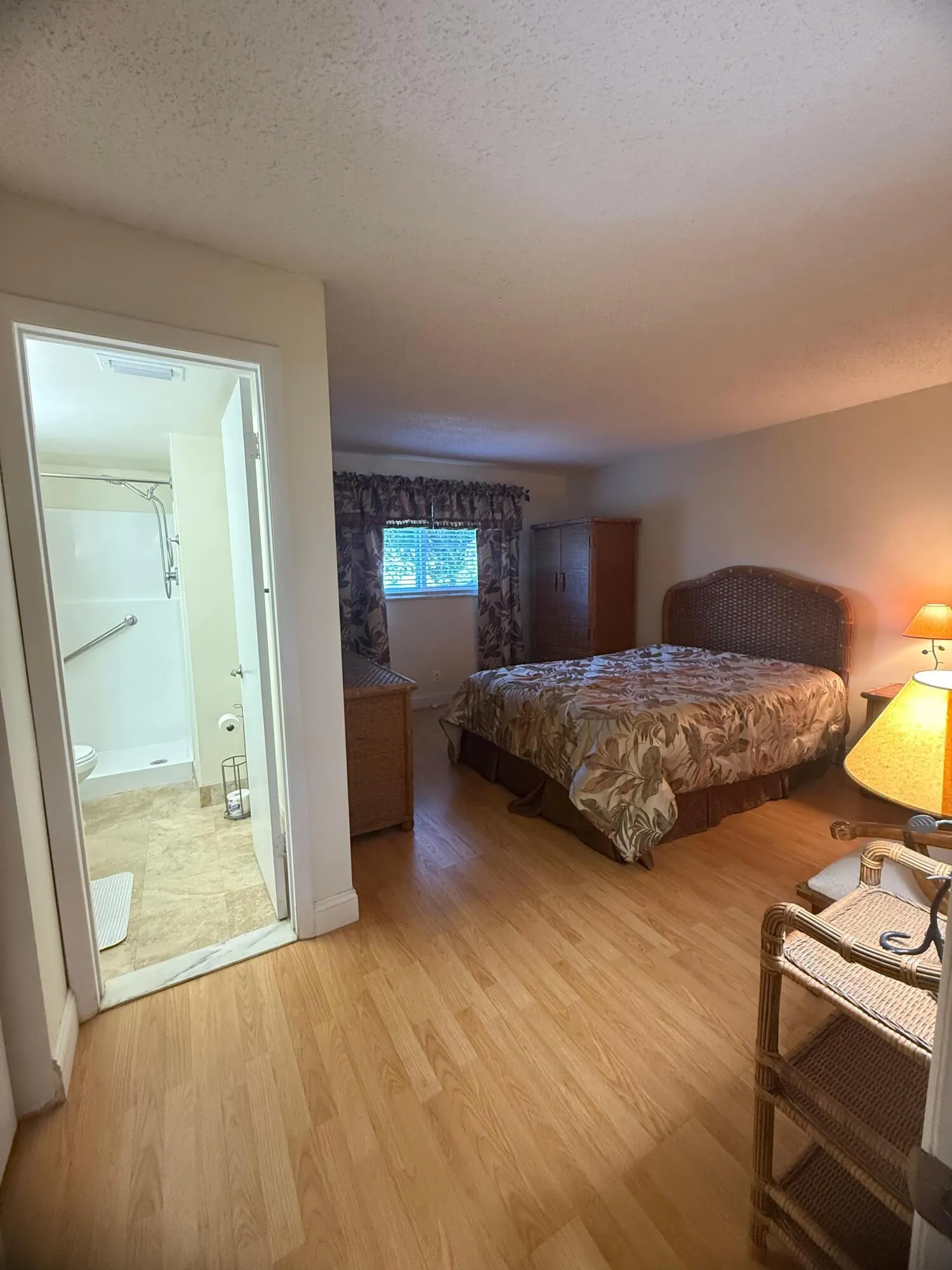 Spacious room featuring wood-finish flooring, a window with valance and drapes, and an attached bathroom with a shower and grab bar