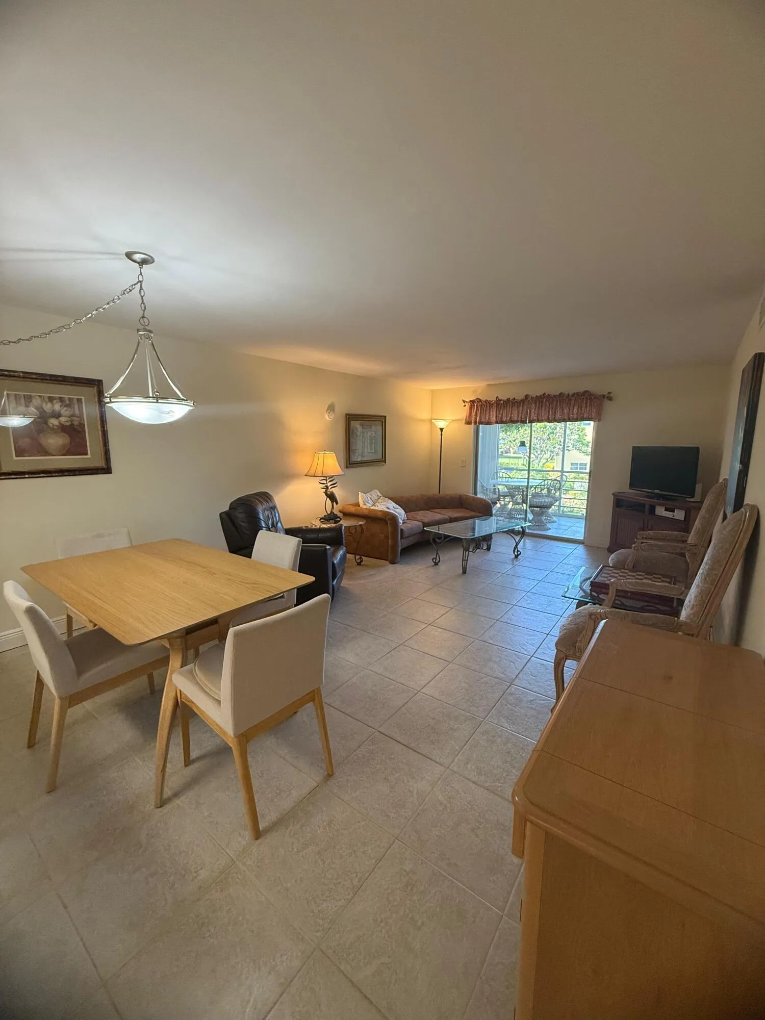 Open-concept living space with tile flooring, a dining area featuring a light wood-finish table, and a living area with a sliding glass door to an outdoor area