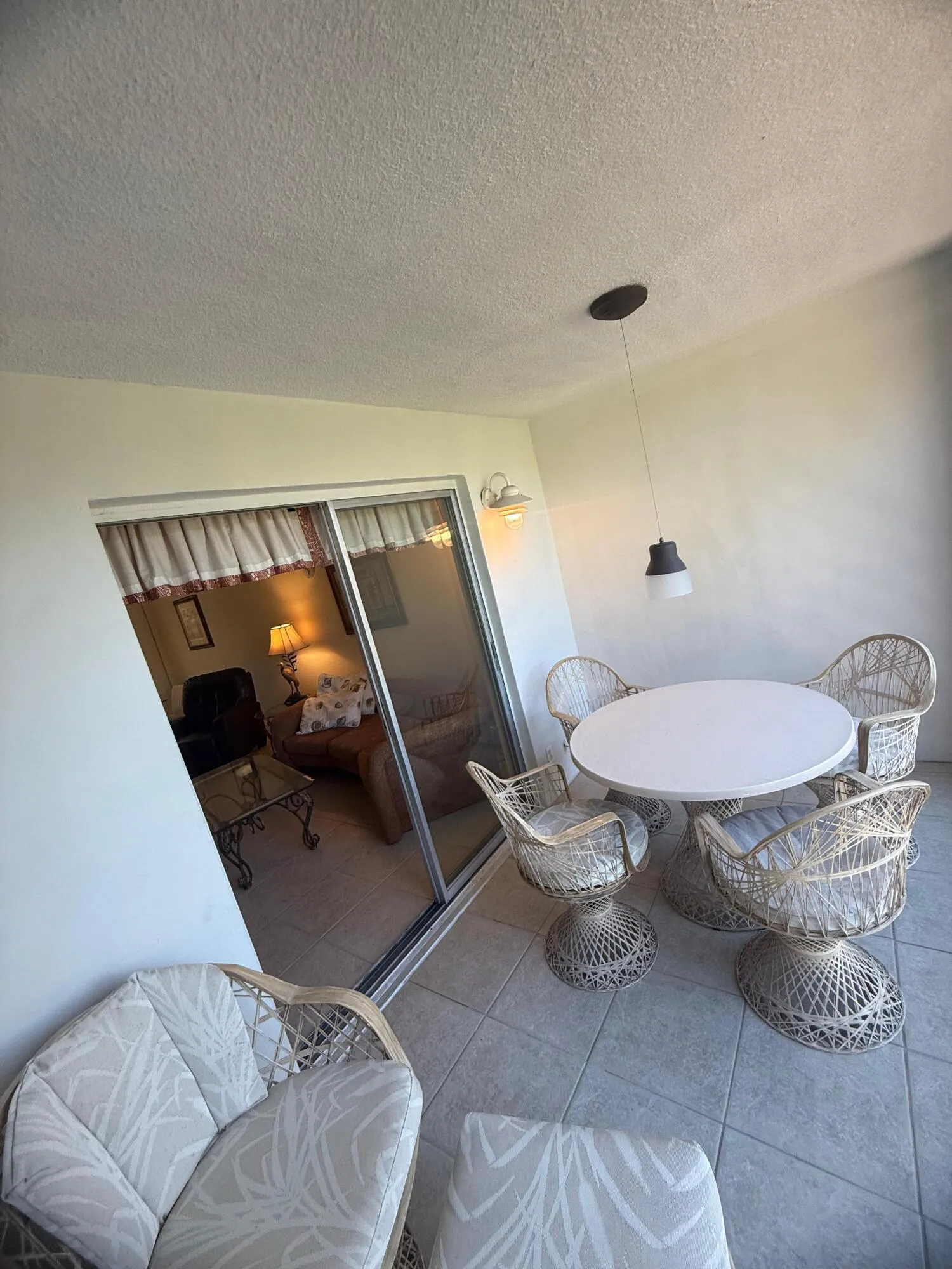 Tiled balcony featuring a sliding glass door entry, ceiling-mounted pendant light fixture, and an exterior wall light