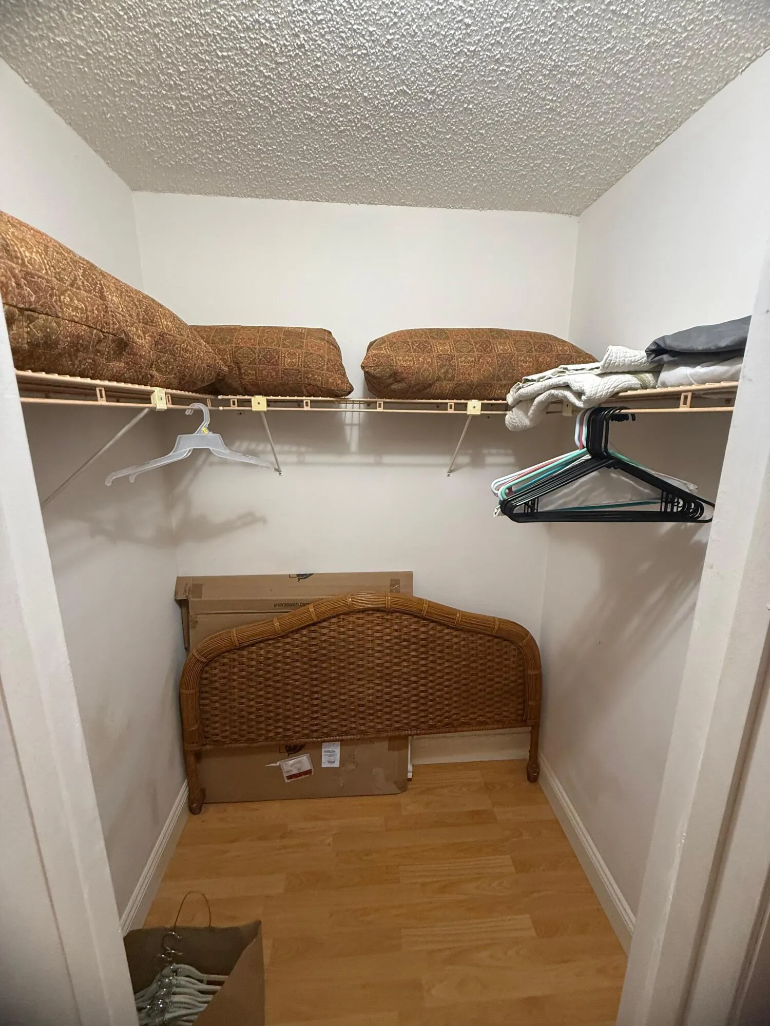 Compact closet with wood-finish flooring, two levels of wire shelving, and white baseboards