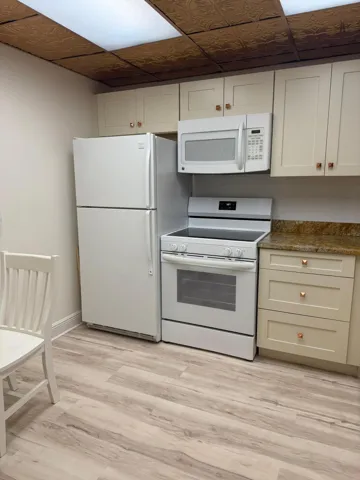 Compact kitchen featuring wood-finish flooring, light-toned cabinetry with copper-toned hardware, a built-in microwave, and a textured ceiling with flush-mounted lighting