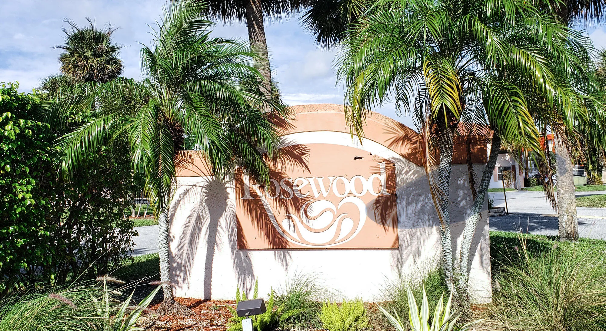 Entry monument with decorative Rosewood signage, complemented by established palm trees and lush tropical landscaping